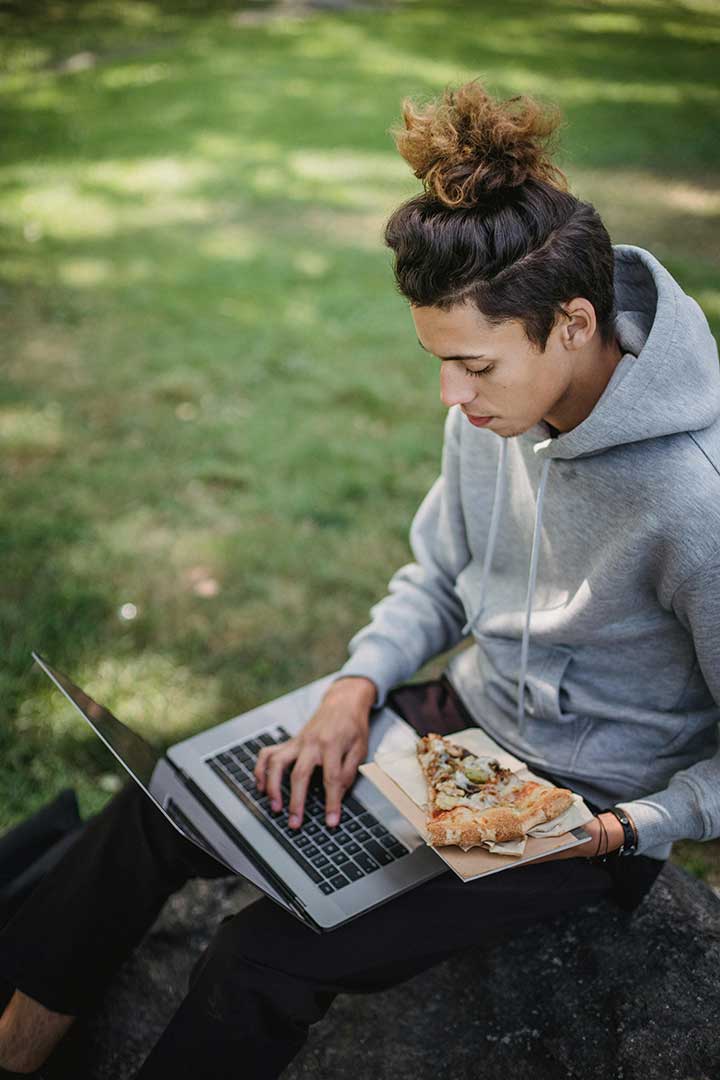 Student on laptop while holding a piece of pizza